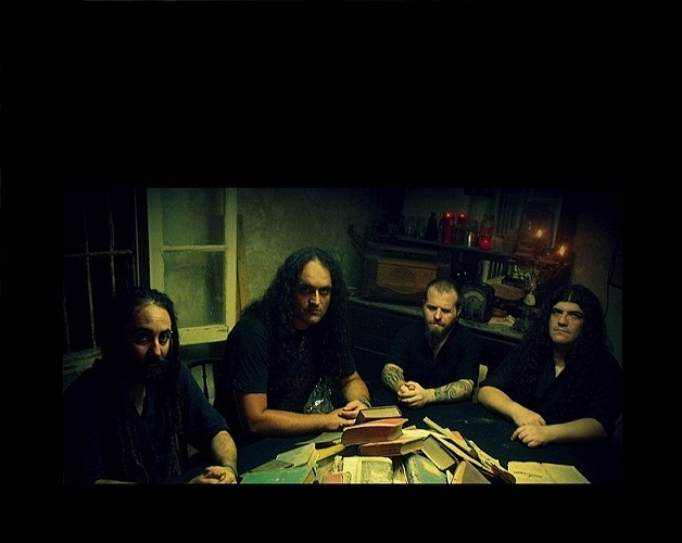 The band seated at a table with candles and old books